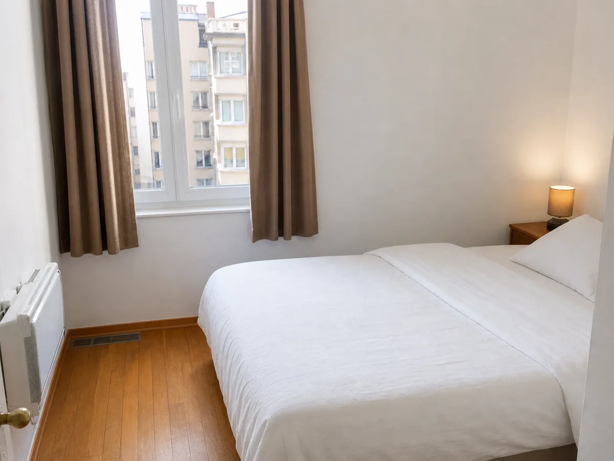 La même chambre après une retouche honnête : lumière naturelle, lit fait, objets temporaires retirés, même vue par la fenêtre