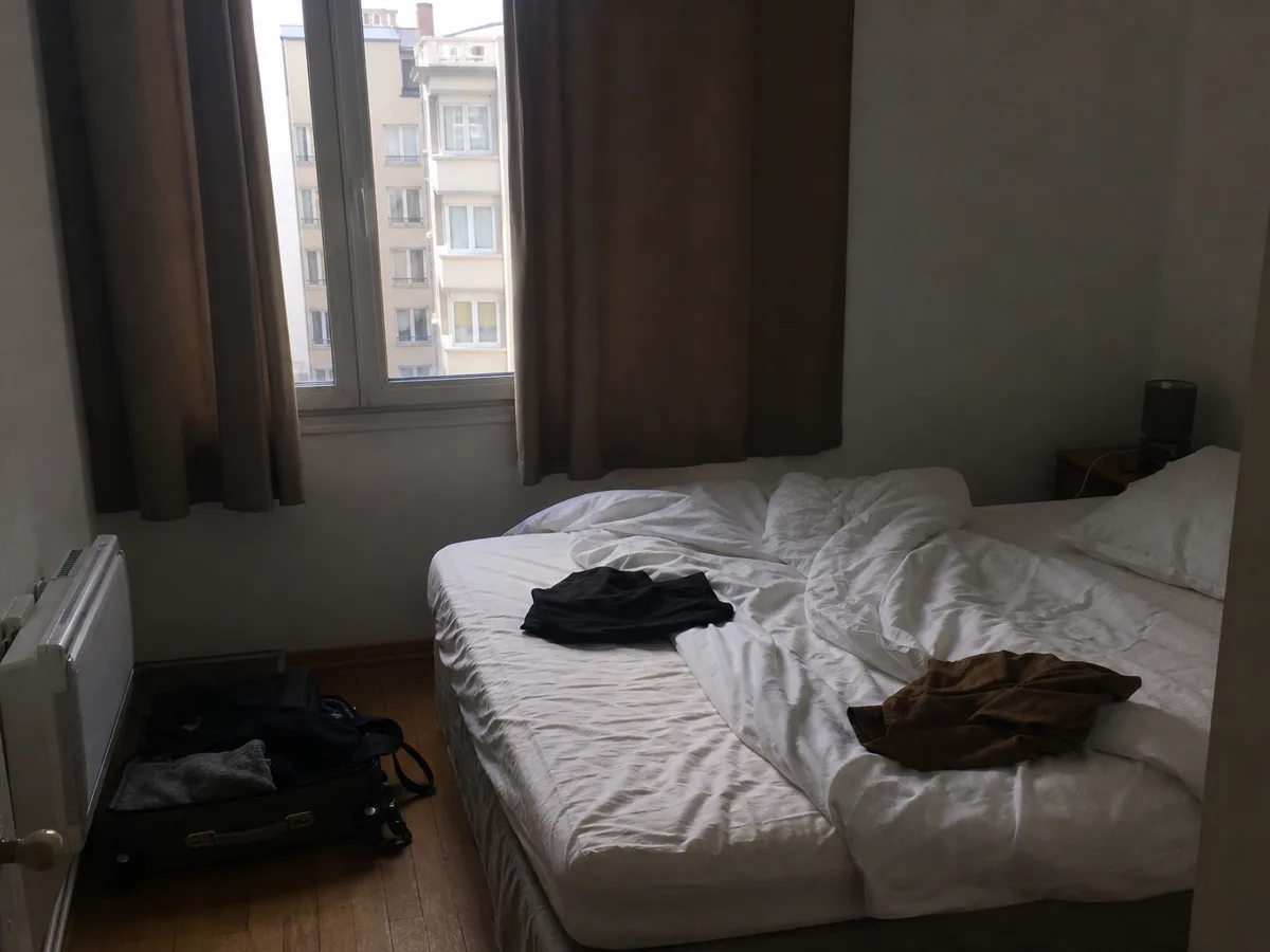 Photo Airbnb typique d'une chambre ratée : sombre, lit défait, valise ouverte et affaires personnelles dans le champ