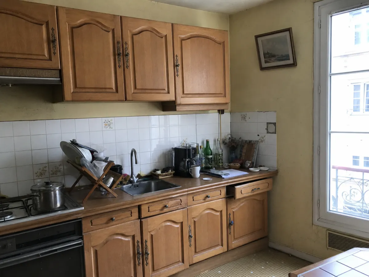 Cuisine encombrée avant home staging : plan de travail surchargé, façades chêne datées, murs jaunis
